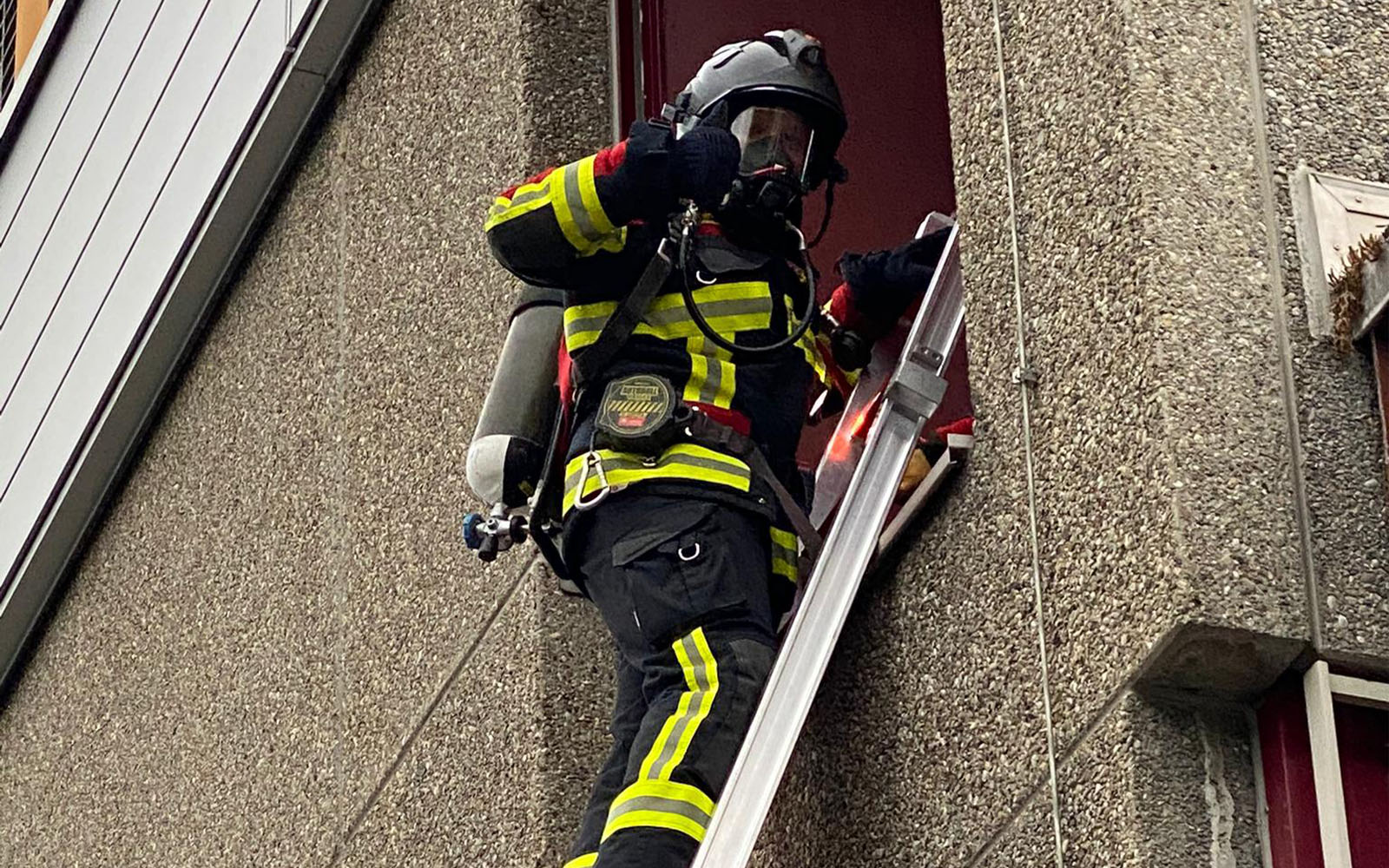 Timo Maibach steht auf einer Leiter, welche an ein Fenster gelehnt ist. Er trägt die volle Atemschutzausrüstung.